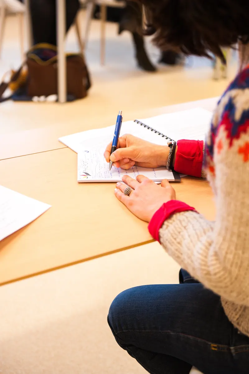 Mano che scrive appunti a penna su un foglio appoggiato al tavolo