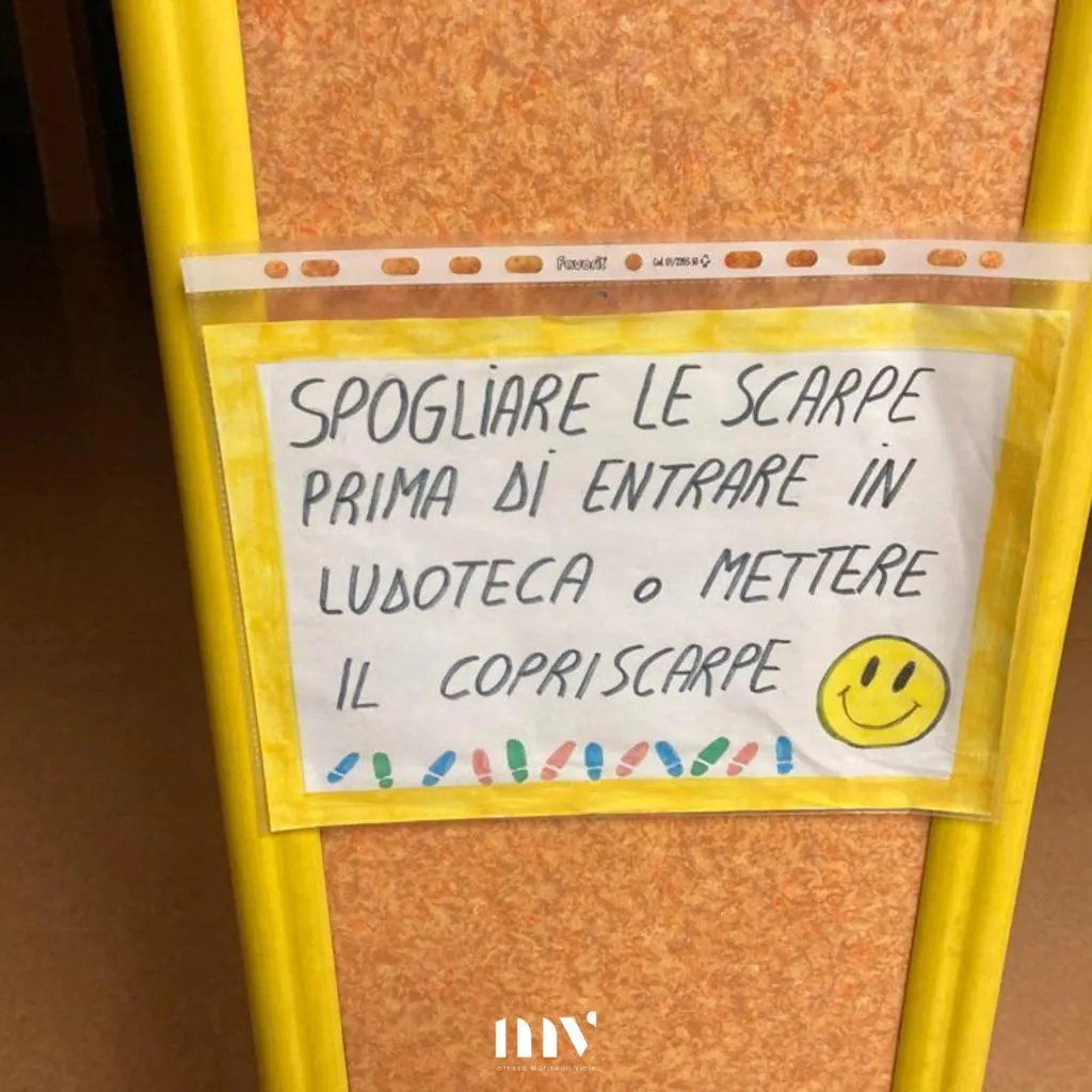 Cartello appeso alla porta della ludoteca: spogliare le scarpe prima di entrare in ludoteca o mettere il copriscarpe