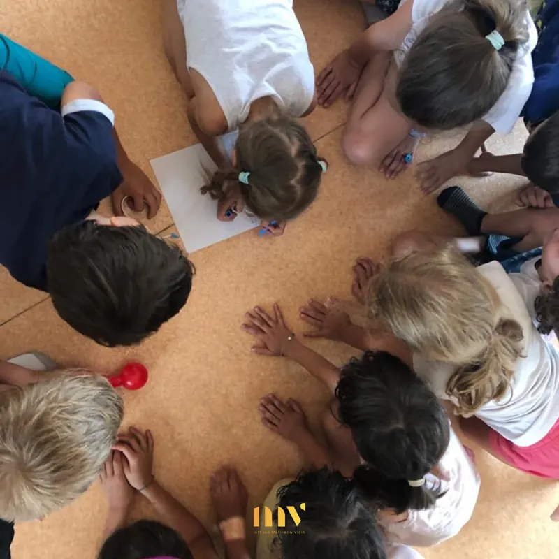 Bambini seduti in cerchio attorno a un grande foglio, visti dall'alto, durante il laboratorio